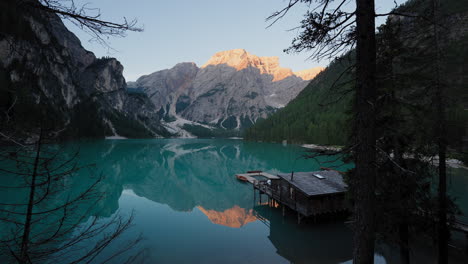panoramic sunrise view of lago di braies with still waters reflecting the dolomites, wooden rowboats moored near the rustic boathouse in perfect alpine serenity