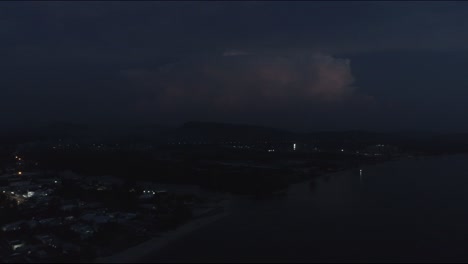 flying backwards away from a big thundercloud flashes lightning up inside in the dark over the ocean coastline