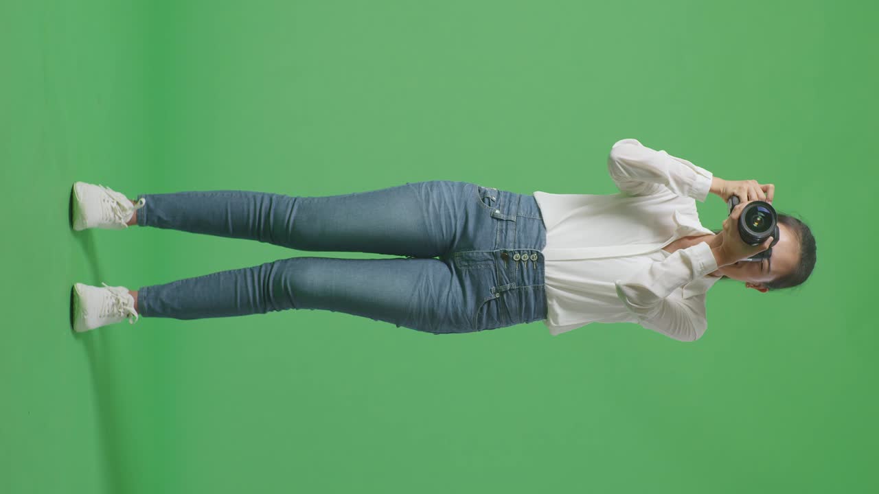 스튜디오에서 녹색 스크린 배경에 서서 사진을 찍고 미소 짓는 카메라를 사용하는 아시아 사진작가의 몸