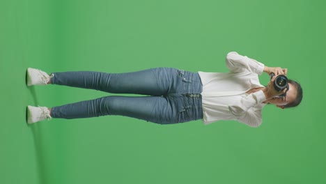 cuerpo lleno de fotógrafo asiático usando una cámara tomando fotos y sonriendo mientras está de pie en el fondo de la pantalla verde en el estudio