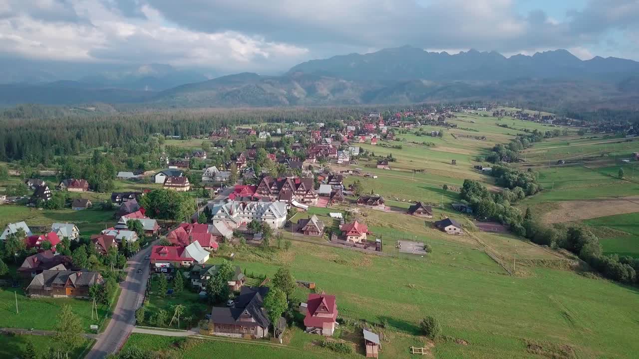 Aerial of small resort in Polish Tatra Mountains. Drone rotates slightly and flies away from the buildings, revealing the majestic mountain range.