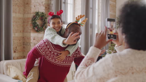 madre tomando una foto de su marido y su hija por el árbol de navidad