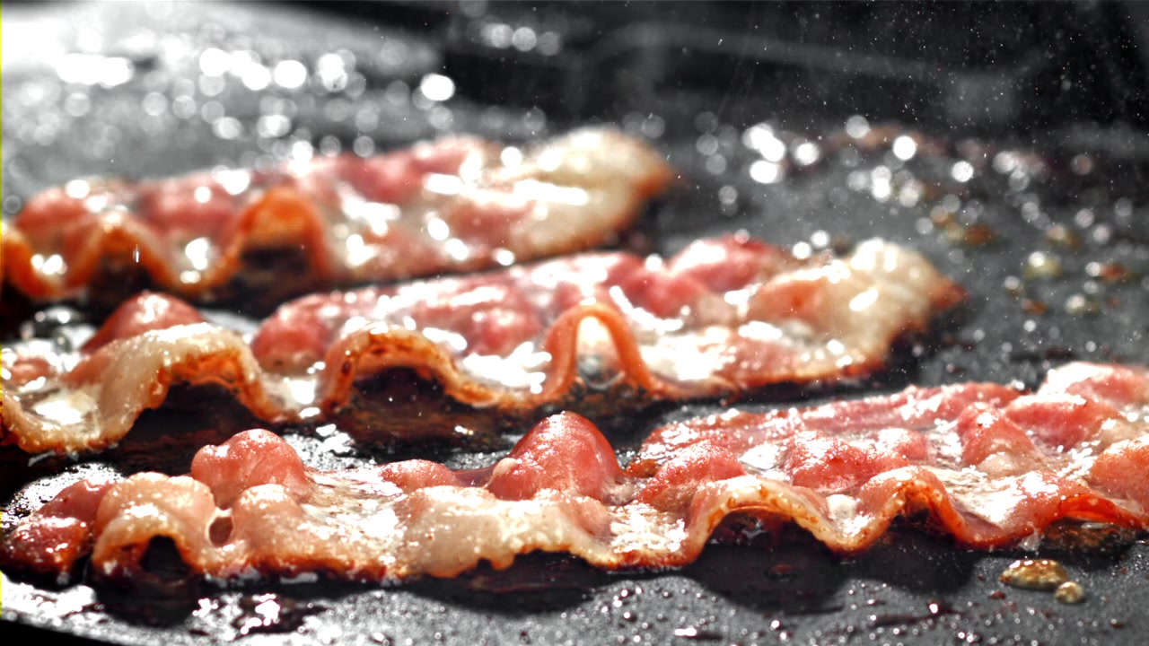 Primo piano di pancetta che sfrigola e frigge su una piastra calda