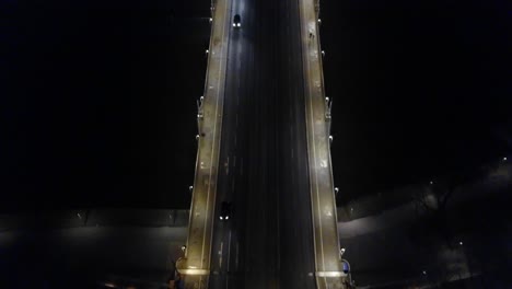 tilting down following a car driving over a bridge untill it stops at the next intersection at night