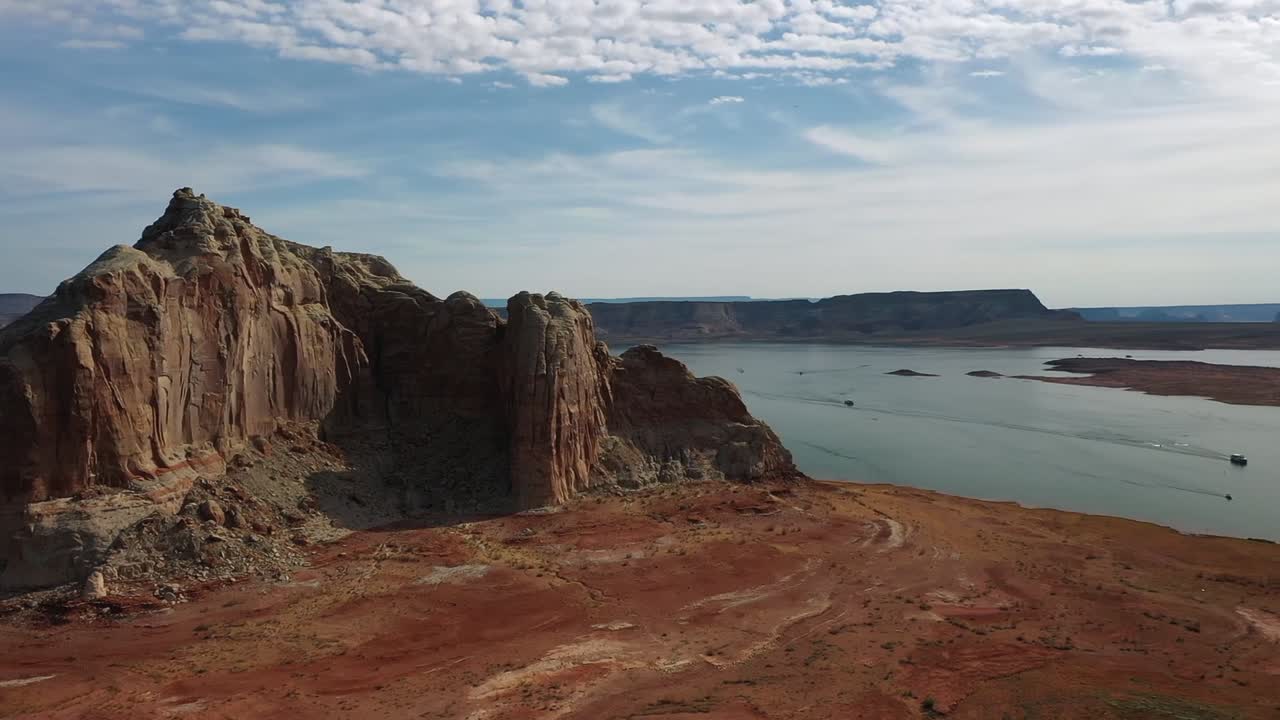 Stunning aerial view captures Lake Powell's vast expanse near Wahweap Bay, highlighting majestic rock formations, vibrant red terrain, and tranquil waters under a cloudy sky