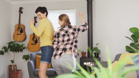 caucasian lesbian couple dancing together in the living room at home