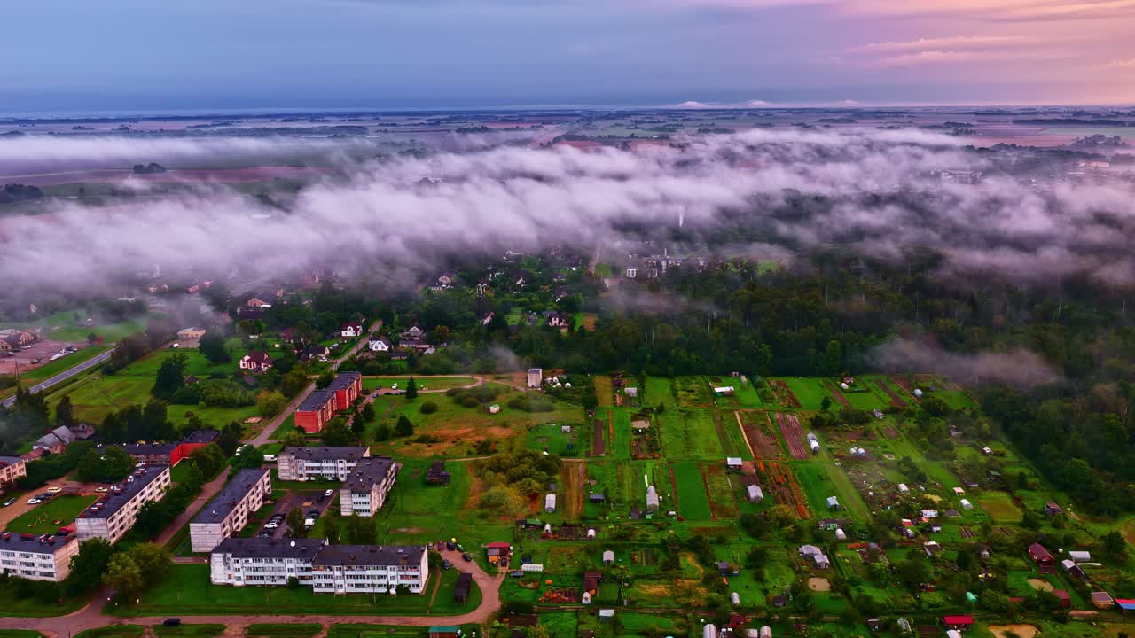 Drone moving along clouds over a green town during sunrise