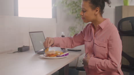 pregnant woman eating chicken nuggets sitting at desk in the office