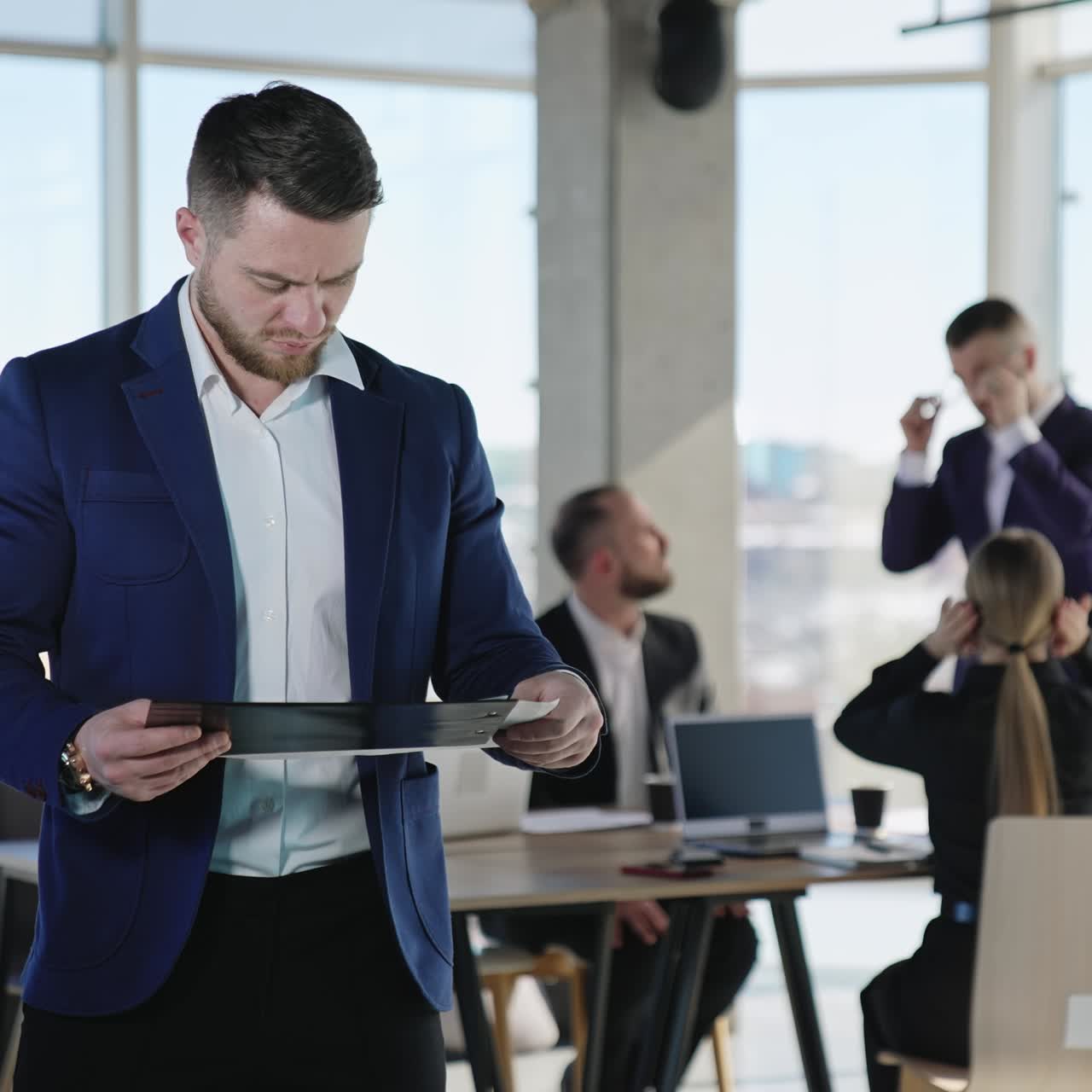 Young businessman holding documents and commenting something in front of camera. Business team working at the backdrop