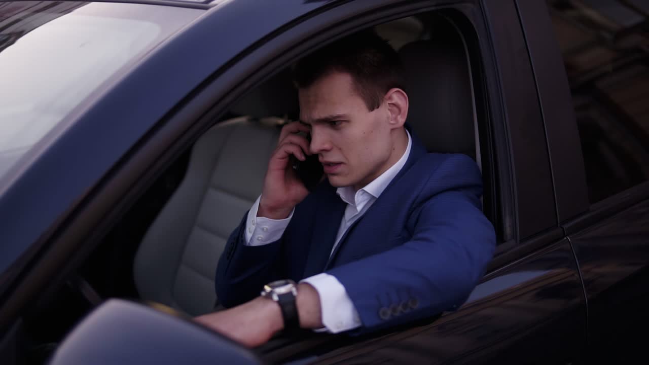 Handsome man sitting in the car on a driver's seat, holding hand on the car door. Businessman talking while sitting in a car
