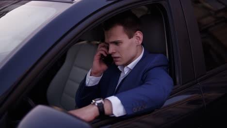 handsome man sitting in the car on a driver's seat, holding hand on the car door. businessman talking while sitting in a car