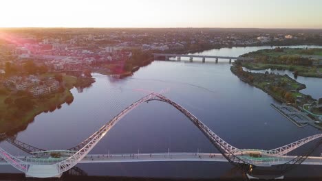 Vista-Aérea-De-Un-Río-Cisne-Con-Movimiento-De-Cámara-Hacia-Atrás-Que-Revela-El-Puente-Matagarup-Con-Gente-Que-Va-Al-Otro-Lado