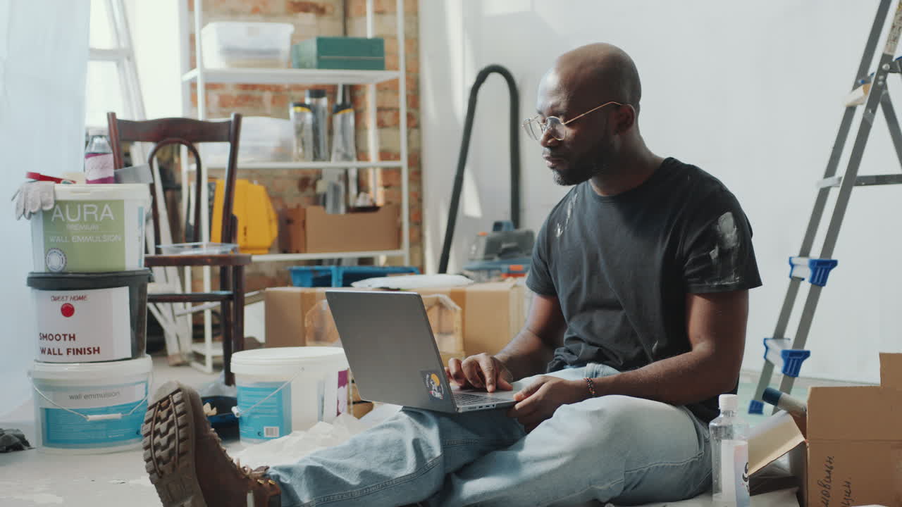Black Man Sitting in Living Room under Renovation and Using Laptop