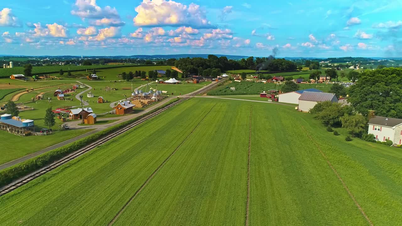 Una vista aerea di campi agricoli Amish con un singolo binario ferroviario e un treno passeggeri a vapore in avvicinamento