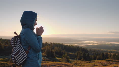 the traveler drinks hot tea on the top of the mountain admiring the sunrise on the horizon nature of