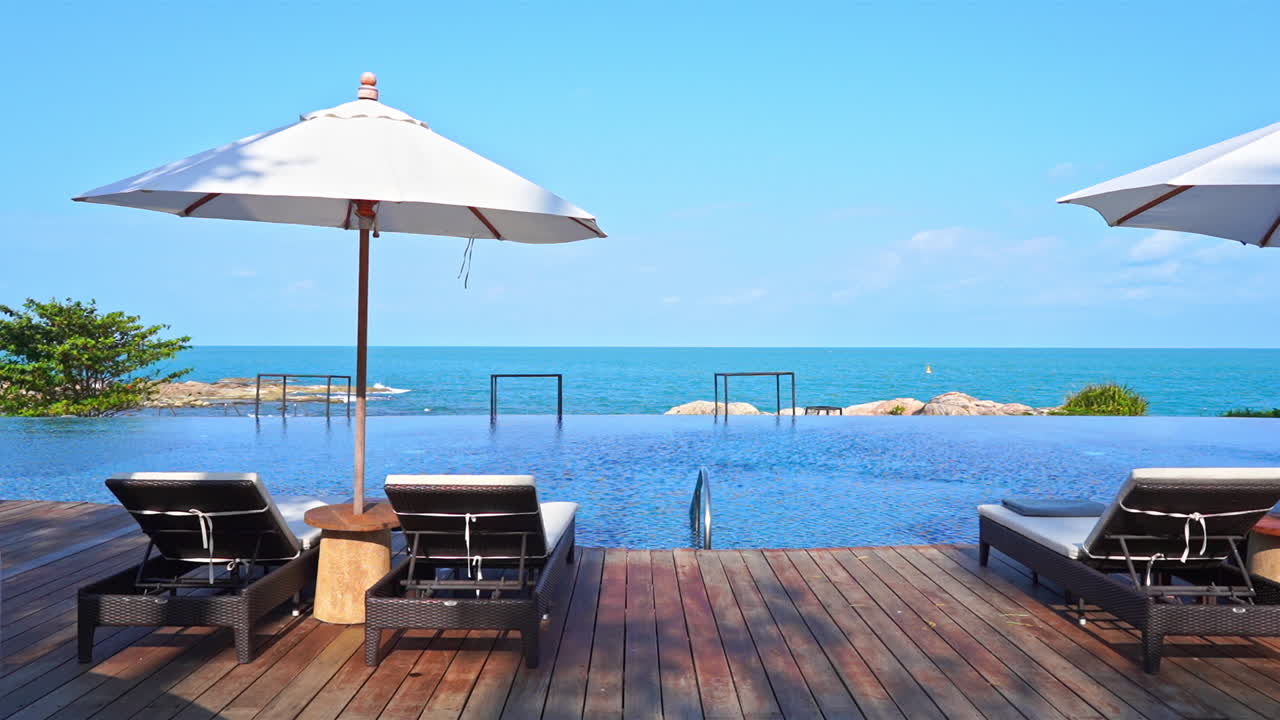 화창한 날 발리의 바위섬에 야외용 데크 의자와 흰색 파라솔이 있는 인피니티 풀 라운지