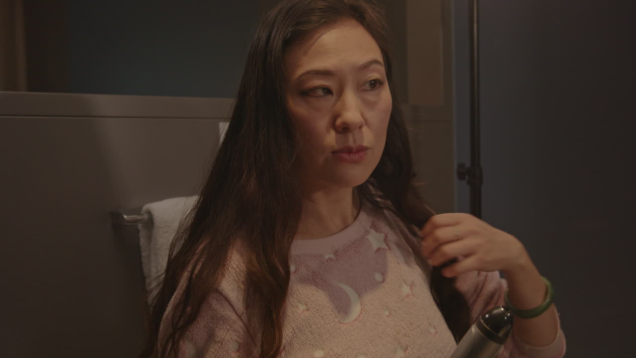 Close up of a pretty Asian woman putting her hair in a curling iron in a hotel bathroom