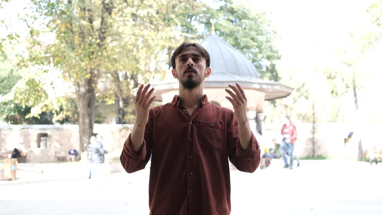 Young bearded Muslim praying with an open hand in the mosque courtyard, people who believe in Islam pray to god