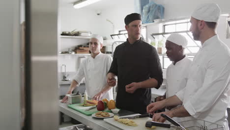 diverse male chef instructing group of trainee male chefs in kitchen, slow motion