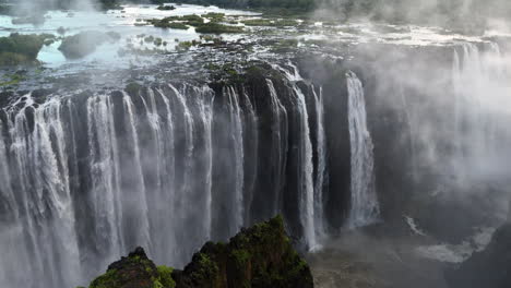 aerial view of victoria falls with powerful waterfall plunging into gorge, mist rising above lush green forest, dramatic natural wonder and iconic travel destination in africa