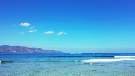 vivid colors of peaceful seascape with white waves foaming on shore of tropical island, blue sea and bright sky background in indonesia