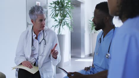 caucasian female senior doctor discussing with diverse male colleagues at hospital staff meeting