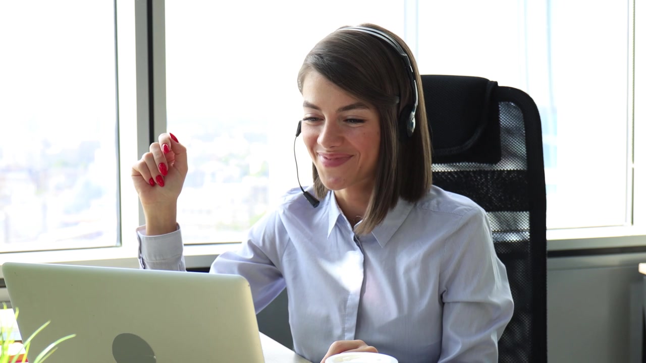 Donna sorridente con le cuffie che lavora al laptop in ufficio