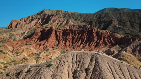 Man-standing-on-canyon-ridge-at-Fairy-Tale-Canyon-near-Issyk-Kul-Lake-in-Karakol,-Kyrgyzstan,-wide-rotating-aerial-drone-shot