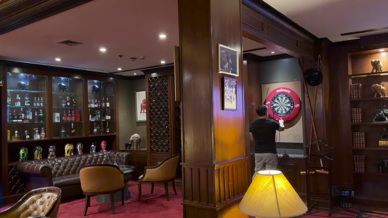 Man playing darts in elegant lounge bar, warm lighting, steady camera, relaxed atmosphere, Bangkok location