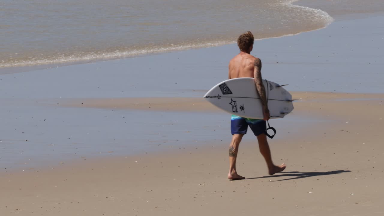 hombre caminando por la playa con una tabla de surf