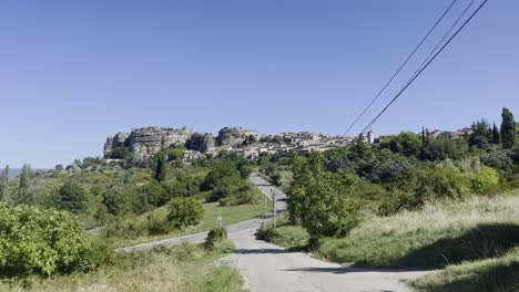 landscape with a road through nature leading to a small historic stone village in strong sun