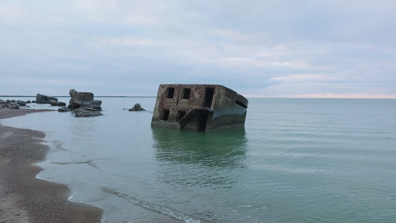 вид с воздуха на заброшенные приморские фортификационные сооружения северных фортов каросты на пляже балтийского моря, плеск волн, пасмурный день, низкий широкий кадр с дрона, движущийся вперед