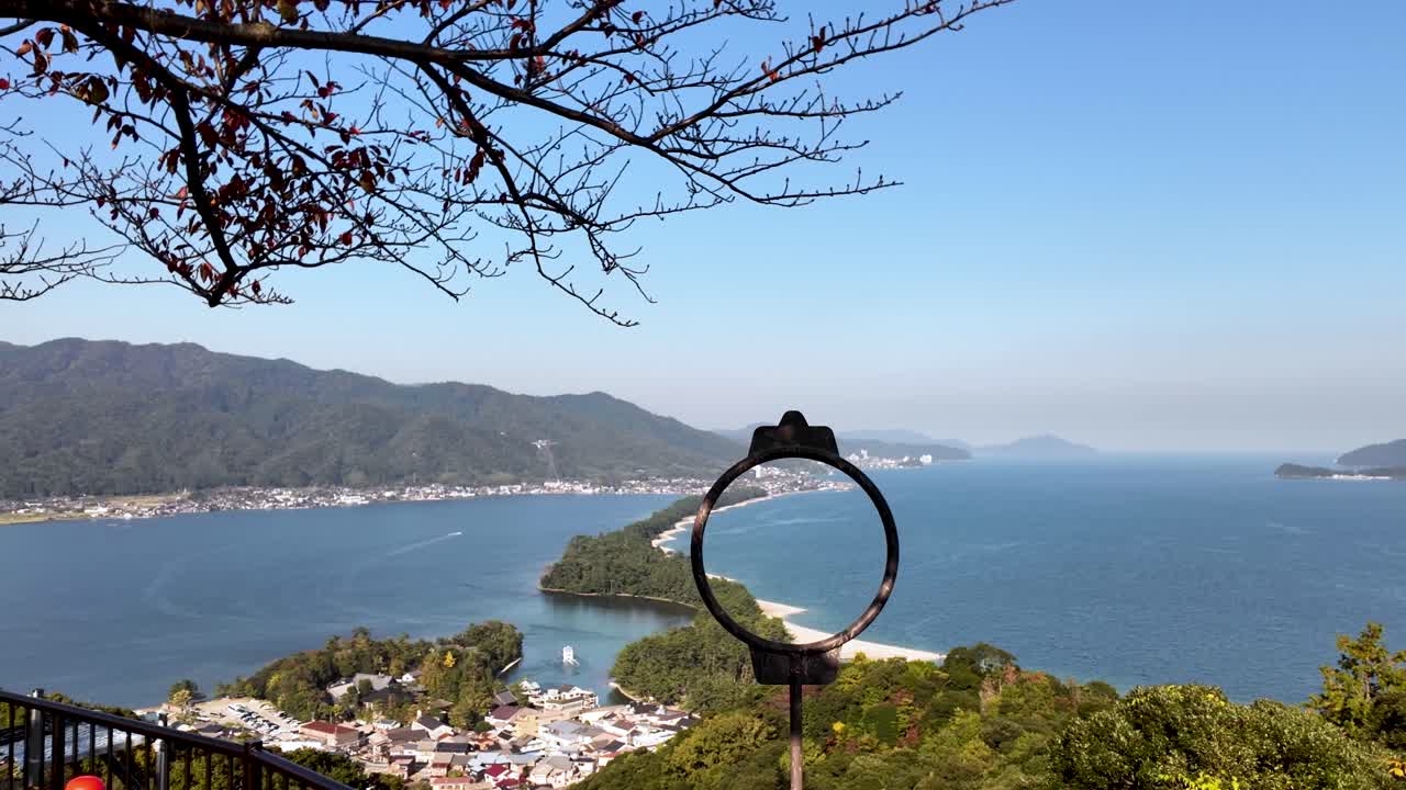 Breathtaking view of Amanohashidate Sandbar framed by circular viewing device, showcasing the picturesque bay, lush greenery, and clear blue sky