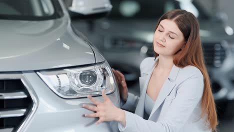 Stylish-girl-sitting-near-a-new-car-kisses-the-bumper-and-hugs