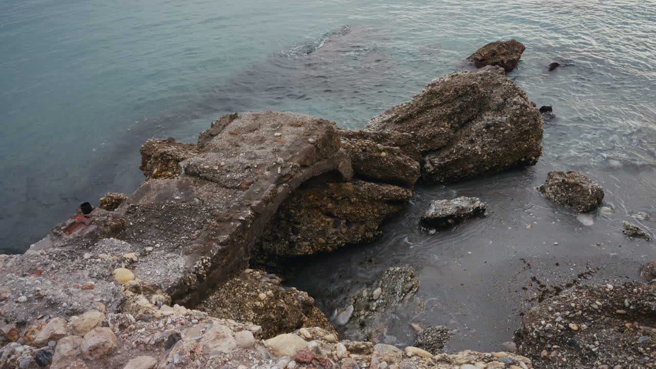 Vista dall'alto di rovine di cemento erose lungo la costa spagnola. Architettura consumata dagli agenti atmosferici incontra rocce aspre e le calme acque del Mediterraneo.