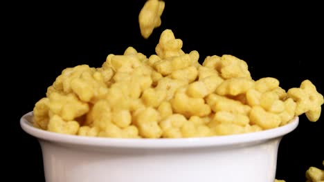 yellow cereal pieces fall into a white bowl against a black background, captured in slow motion with clear lighting