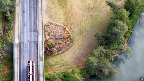 overhead drone footage captures two trucks traveling across a country bridge above a river in coonabarabran, nsw, under soft daylight with steady camera movement