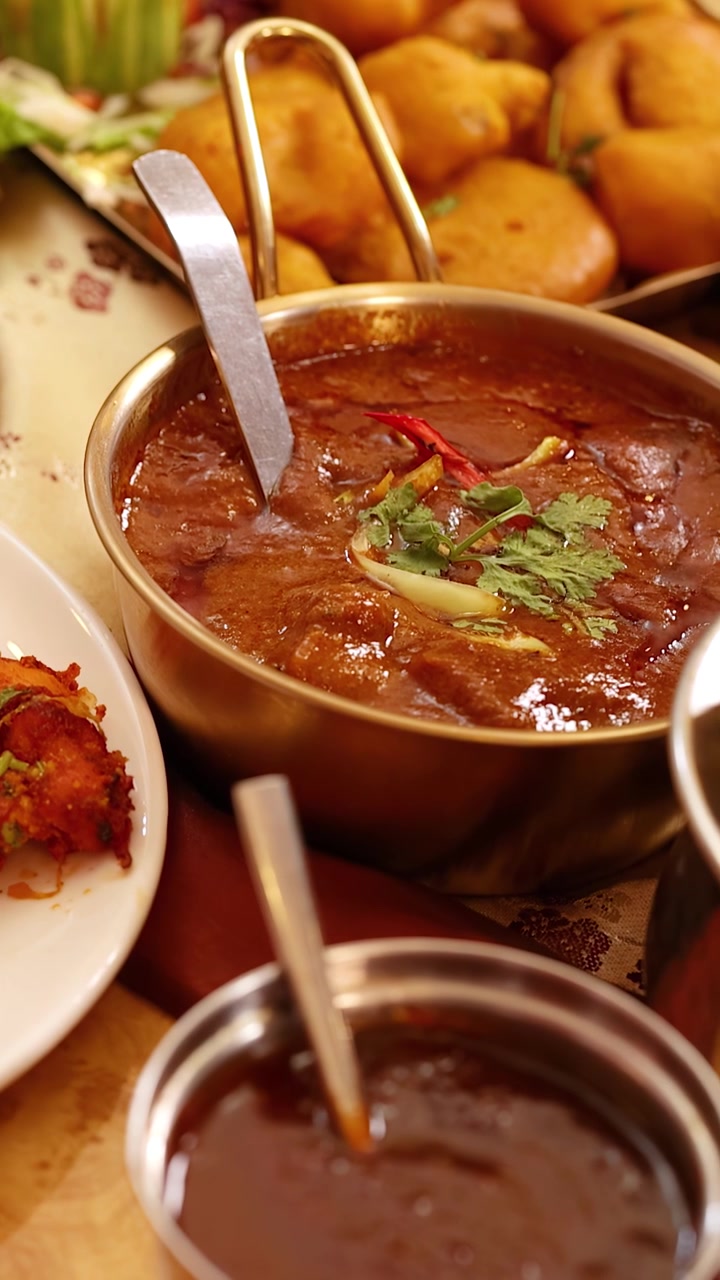 Primo piano di una persona che mangia cibo indiano, inclusi curry, naan e pollo tandoori, a Bangkok