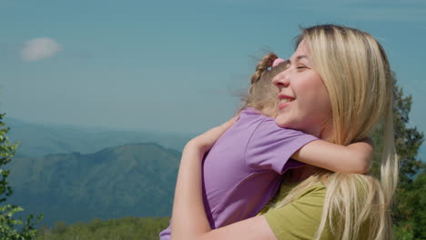 Joyful-woman-holds-little-daughter-against-old-mountains