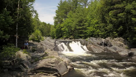 pulling away from a waterfall with a man sitting beside it on the river bank