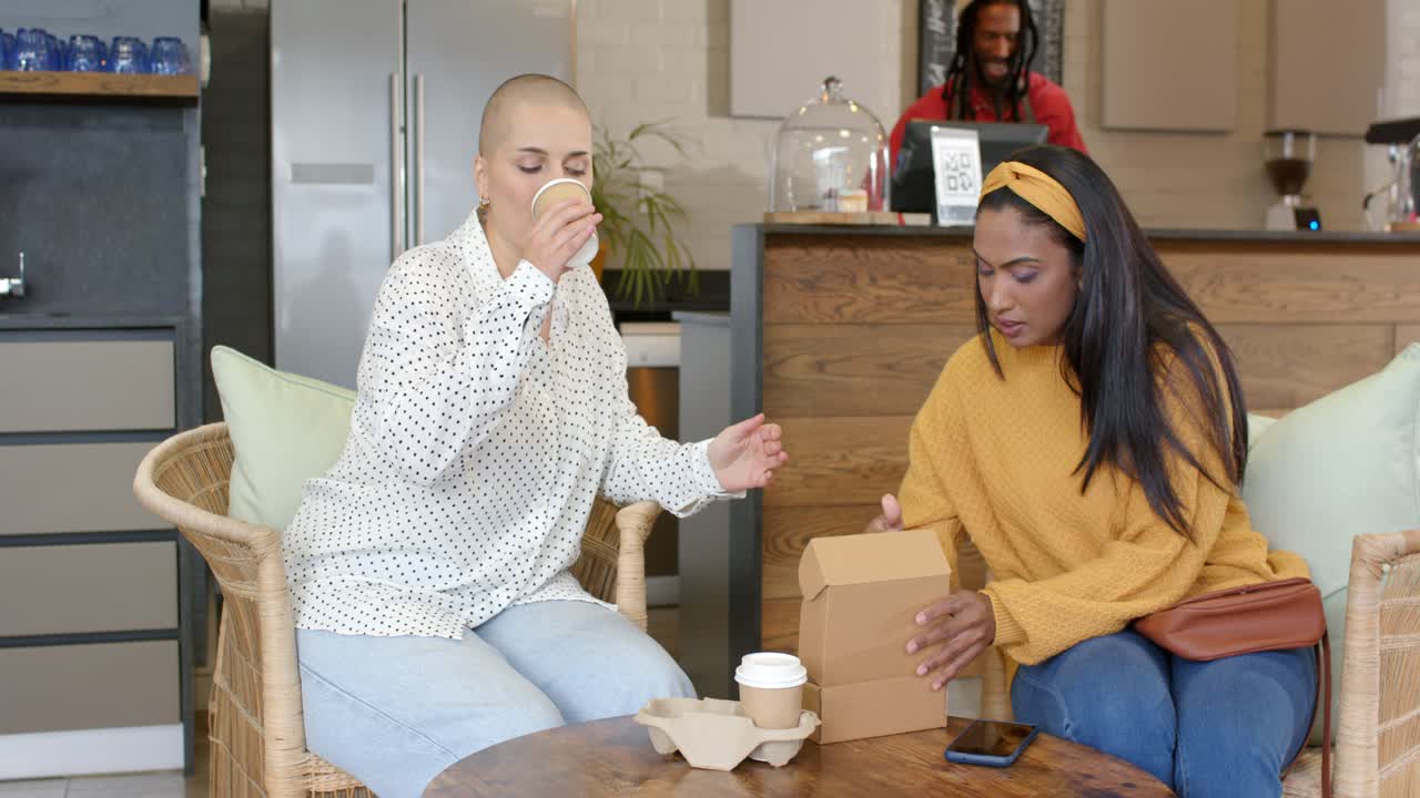 Diverses amies plaçant une boîte de plats à emporter et tapotant sur un smartphone avant d’ouvrir le couvercle à une table de café