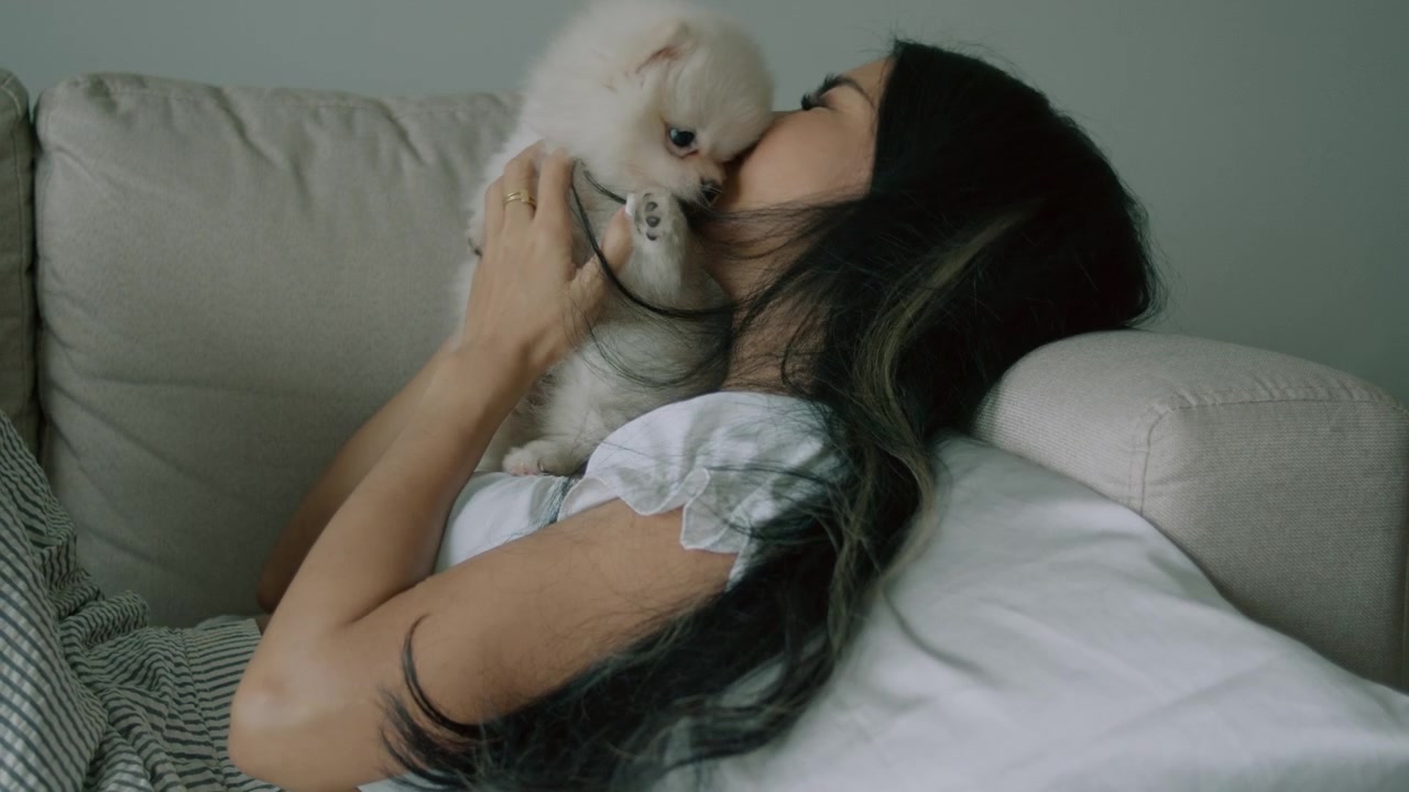 Giovane donna che coccola il suo soffice cucciolo di Pomerania sul divano
