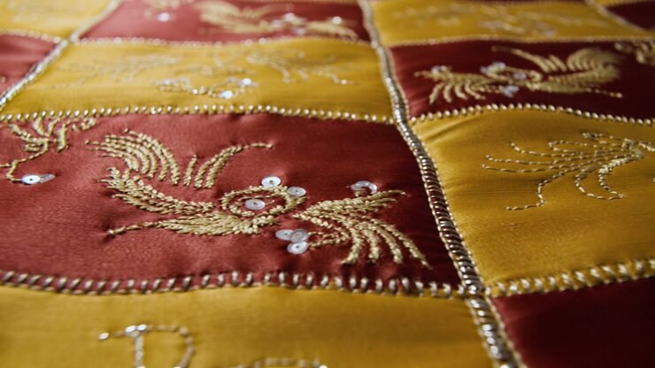 Messa a fuoco a cremagliera rivela un tessuto patchwork ricamato su un letto, mettendo in risalto fili d'oro e paillettes.