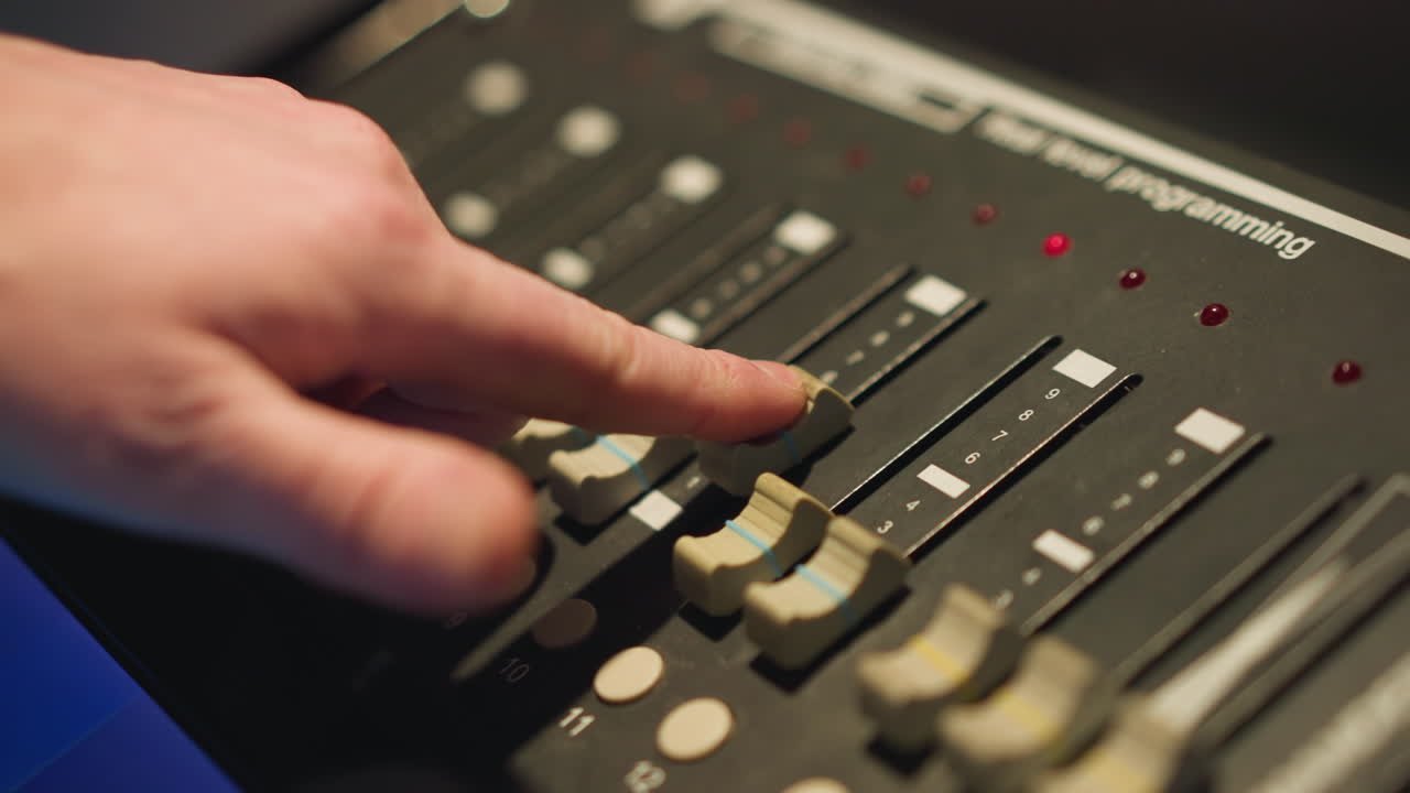 Close-up of person adjusting fader and switches on lighting control panel, fine-tuning settings, working with equipment for stage or studio light management, controlling light intensity