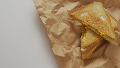 Video-of-close-up-of-toasted-cheese-sandwiches-on-brown-paper-over-grey-background