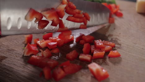 Woman-chopping-up-red-pepper,-capsicum,-bell-pepper-on-wooden-chopping-board,-slow-pan-right-to-left-close-up