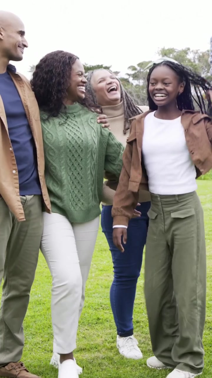Vertical video: Coming pair sparking family linking arms walking on lawn in jackets, mask on chin