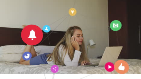 animation of network social media icons over smiling relaxing on bed using laptop