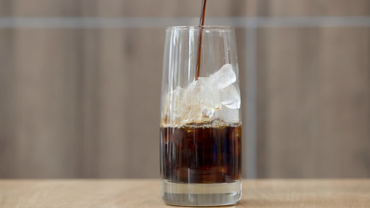 Café negro oscuro vertido sobre cubitos de hielo en un vaso alto.