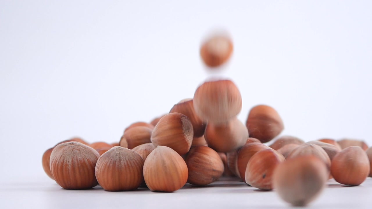 Whole Hazelnuts Dropping and Rolling on White Surface